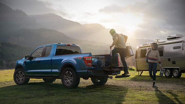 A man climbing in the bed of a Ford F-150, and a woman at a campsite with an RV in the background.